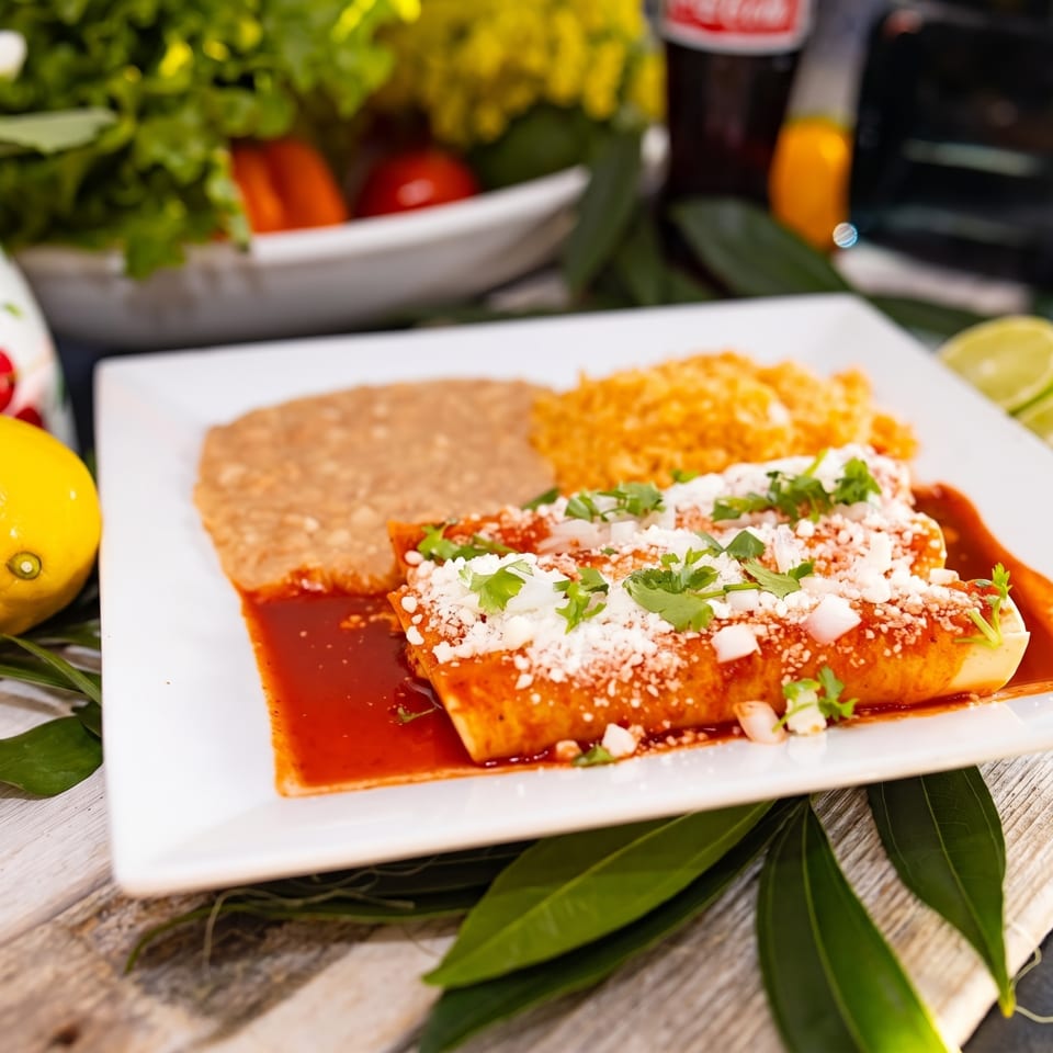 A plate of enchiladas with rice and beans, garnished with cilantro and cheese, on a wooden table.