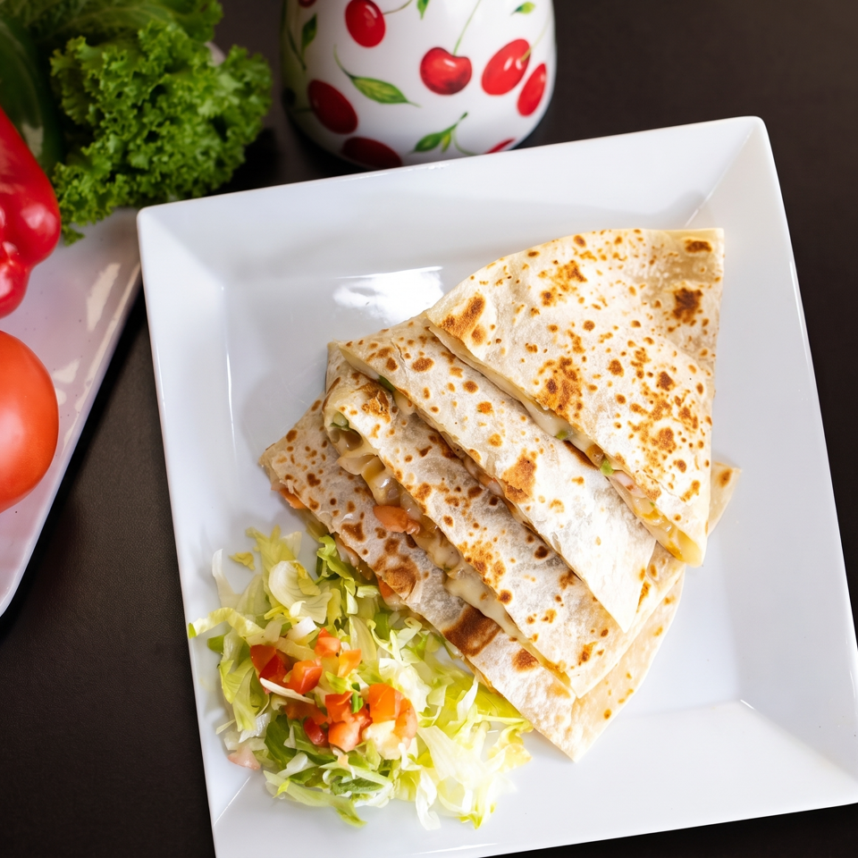 Four quesadilla wedges with melted cheese and green onions, served with a side salad.