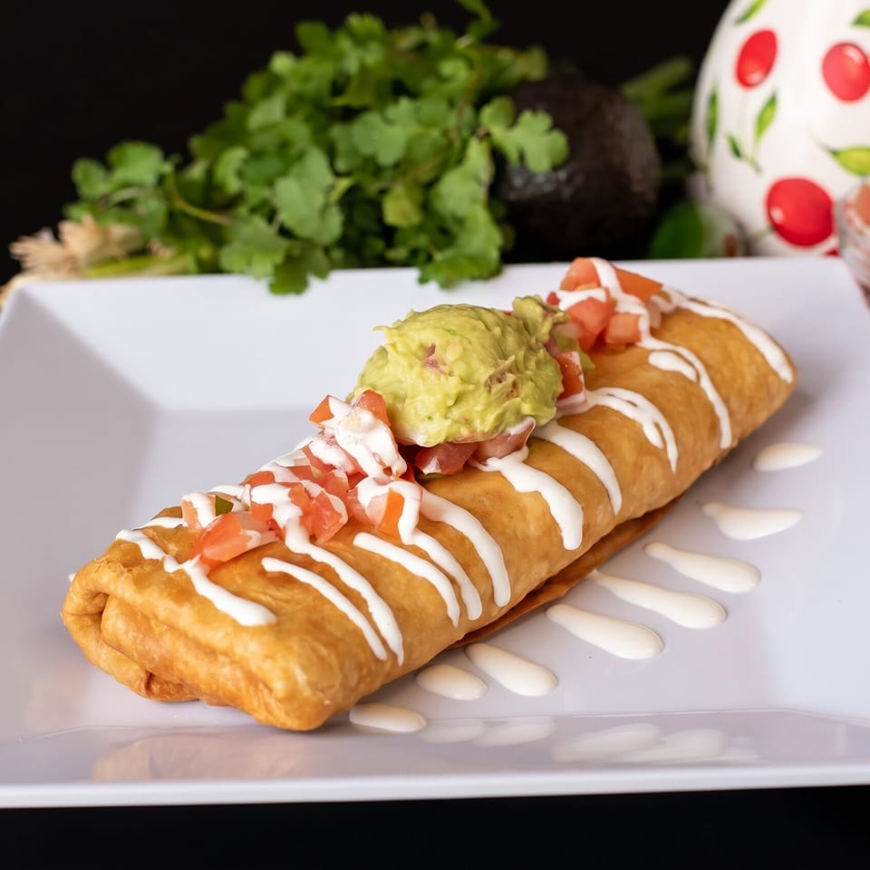 Golden-brown deep-fried burrito topped with guacamole, diced tomatoes, and a drizzle of sour cream.