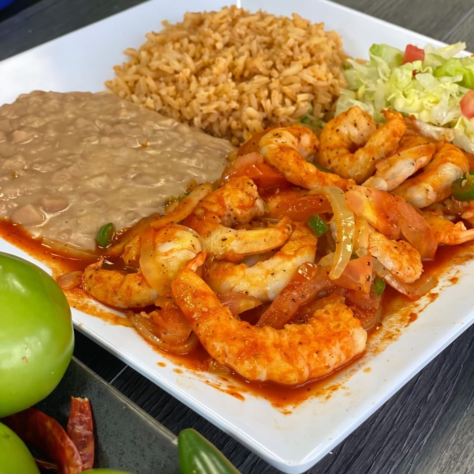A plate of shrimp in red sauce with rice, refried beans, and a side salad.