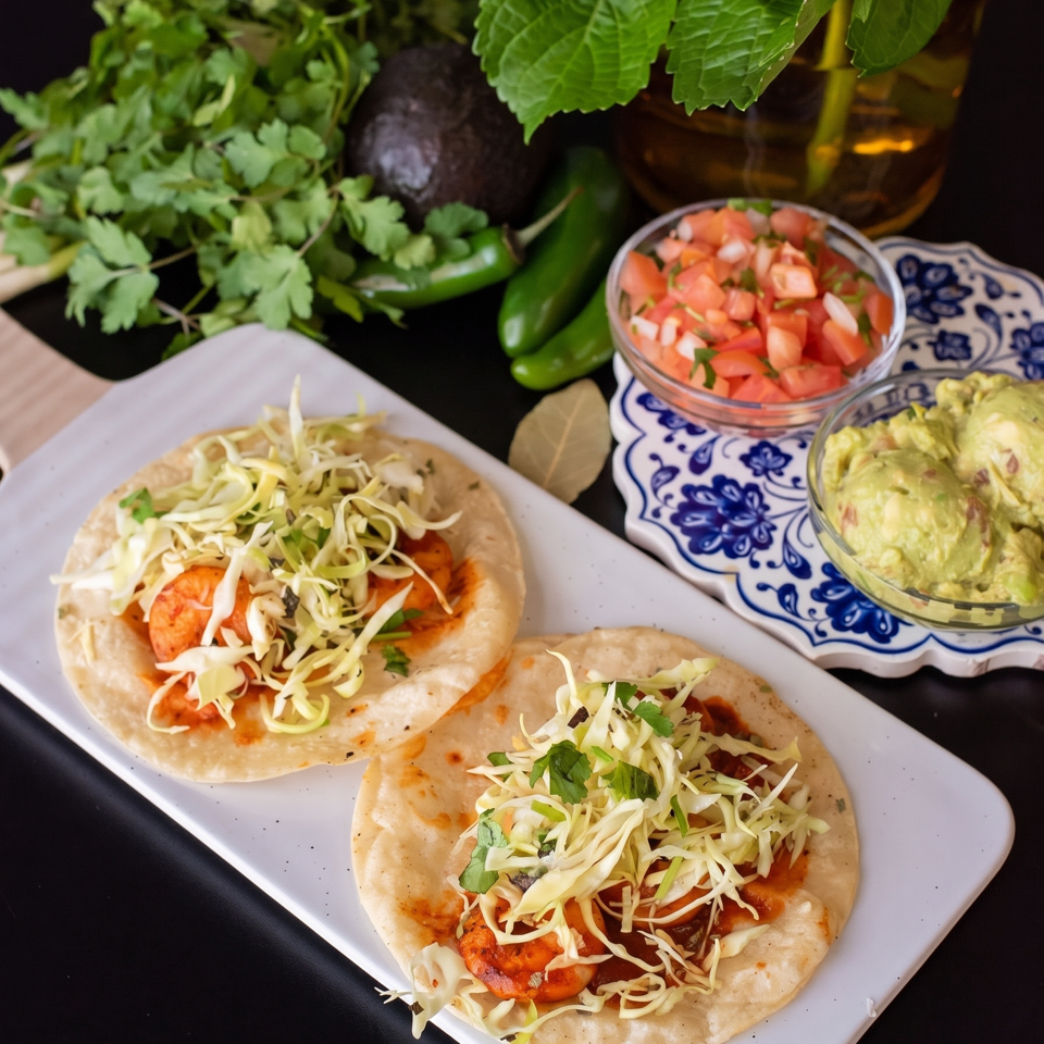 Two shrimp tacos with shredded cabbage and cilantro, alongside guacamole and pico de gallo.
